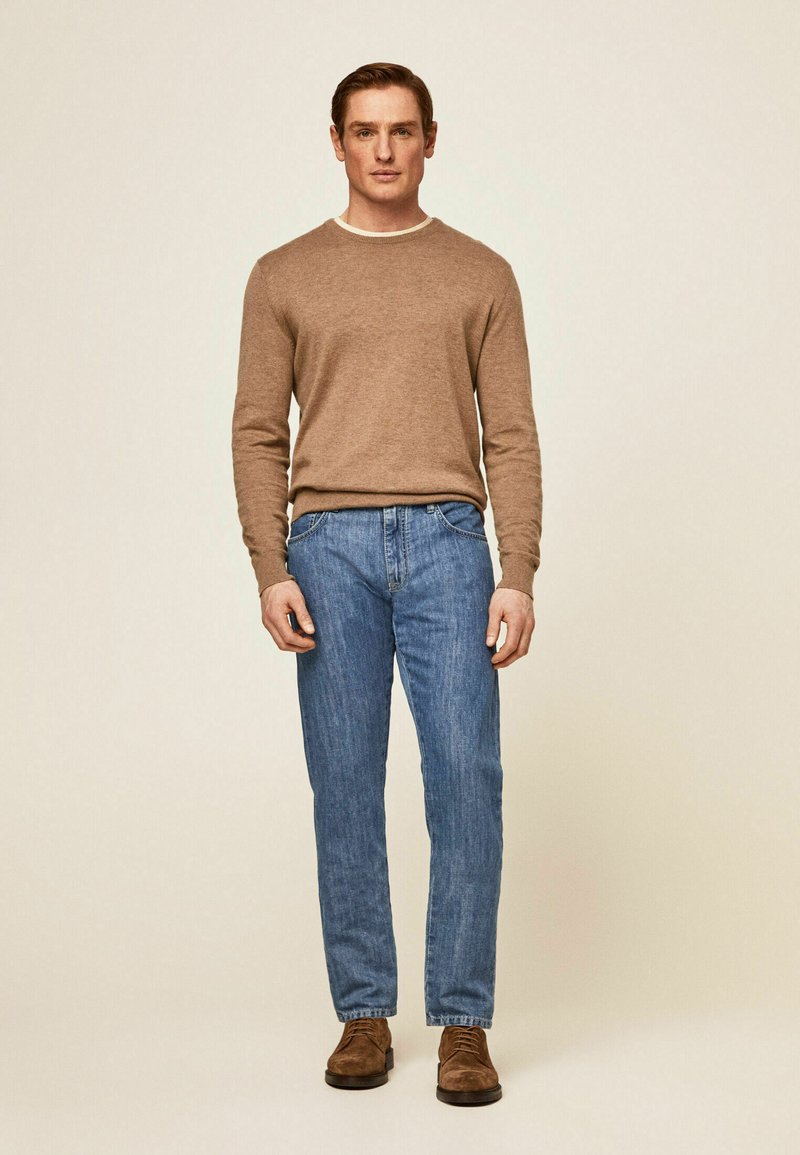 Suéter de punto marrón claro, jeans de denim azules, zapatos de ante marrones. Diseño sencillo con un detalle de cuello y corte clásico.