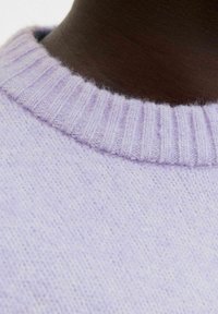 Světle fialový pletený svetr s ribbovaným výstřihem a jemnou strukturou, s nenápadným vzorem v přízi. Zaměření na řemeslné zpracování a barvu.