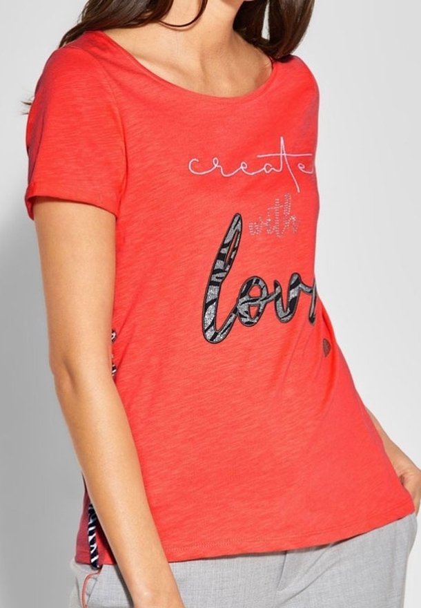 Červené tričko s krátkým rukávem s nápisem "tvořte s láskou" v černé a stříbrné barvě, s detaily vzoru na bocích a z měkké, lehké tkaniny.