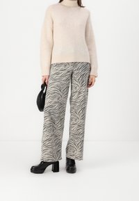 Jasno beżowy sweter z wysokim kołnierzem, zestawiony z szerokimi spodniami w szary zebra print. Całość uzupełniają czarne buty na platformie i torebka.