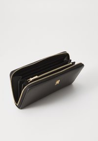 Black leather wallet with gold zipper, featuring multiple compartments and a small logo emblem on the front. Smooth texture, rectangular shape.