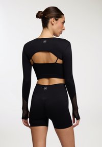 Czarna sportowa bluzka z długimi rękawami i wycięciem na plecach, zestawiona z czarnymi szortami o wysokim stanie. Posiada siateczkowe akcenty na rękawach.