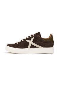 Sneaker in suede marrone con cuciture e lacci bianchi, caratterizzata da un design a croce prominente e un accentuato tallone verde a contrasto. Suola in gomma bianca.
