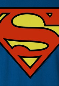 Blaues T-Shirt mit einem großen roten und gelben Superman-Logo, schwarz umrandet, das prominent in der Mitte platziert ist. Weiche Textur.