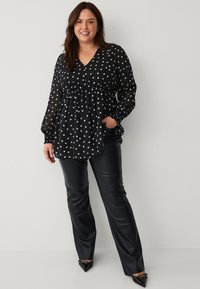 Zwarte blouse met lange mouwen en witte stippen, v-hals, met een gathered taille. Gepaard met gladde zwarte leren broek en puntige zwarte schoenen.