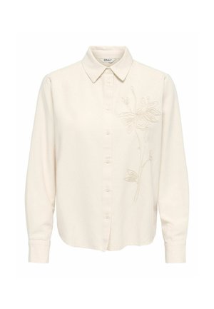 Chemise crème à manches longues avec col et broderie florale subtile sur le côté droit.