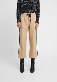 Pantalons larges beige avec une finition texturée, présentant des rayures latérales noires et une taille à cordon de serrage, associés à une chemise noire à motifs à boutons.