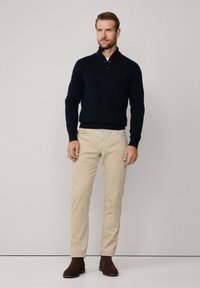 Granatowy sweter dziany z trzema guzikami przy kołnierzu, zestawiony ze jasnobeżowymi chinosami i brązowymi botkami za kostkę; gładka tekstura.
