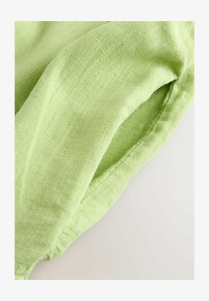 Tissu en lin vert clair avec une surface texturée, présentant de doux plis et un léger éclat. Le bord est cousu avec une finition soignée.