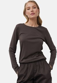 Braunes langärmliges Oberteil mit rundem Halsausschnitt und geripptem Muster, kombiniert mit dunkel gestreiften Hosen. Schlichtes Design mit minimalem Branding.