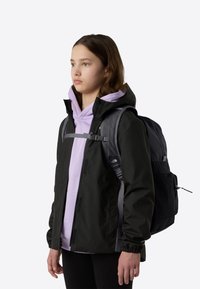 Must veekindel jope helelilla kapuutsiga dressipluusi, mustade retuuside ja aktsentidega halli seljakotiga. Lihtne disain, nähtavaid mustreid ega logosid pole.