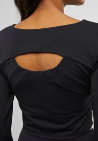 Mustrained musta pikkseeliku varrukatega topp, millel on ümar kaelus ja lõikega detail taga, kogudega aksessuaarid külgedel. Sile kangastekstuuri.