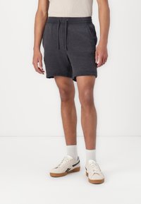 Mørkegrå shorts i et tekstureret stof, midt på låret længde, med en elastisk talje og snor. Båret med hvide sneakers og sokker.