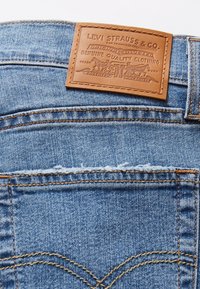 Blugi din denim albastru, având o pată de piele cu un logo în relief. Cusăturile vizibile și detaliile buzunarului din spate îmbunătățesc designul.