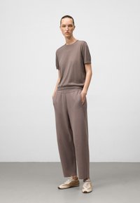 Vrouw die met haar handen in haar zakken staat, gekleed in een bijpassende, relaxte mauve top met korte mouwen en een wijde broek, met beige en witte sneakers.