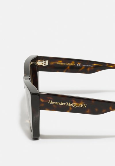 Tortoiseshell sunglasses with a chunky black frame, featuring gold lettering on the temples. Made in Italy, with a sleek, glossy finish.