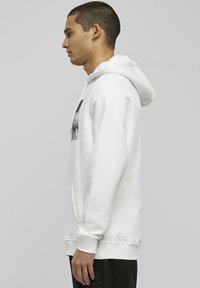 Weißer Pullover mit Kapuze aus weichem Stoff, mit einer Fronttasche und grafischem Druck auf der Brust, sowie einer Kapuze mit Kordelzug und gerippten Bündchen.