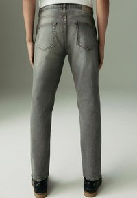 Szare dżinsy o prostym kroju nogawki, z dwoma tylnymi kieszeniami i kontrastowym przeszyciem. Tkanina ma delikatną teksturę.