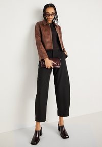 Smeđi kožni skraćeni jakna, crni top, široke crne hlače, bordo clutch s hardverom i sjajne crne štikle.