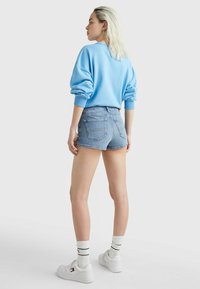 Felpa oversize azzurro chiaro con maniche arrotolate, abbinata a pantaloni corti di jeans a vita alta. Sneakers bianche e calzettoni a righe completano il look.