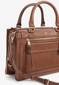 Sac à main en cuir marron avec deux poignées, quincaillerie dorée, accents de couture blanche, une poche frontale zippée et une bandoulière réglable.