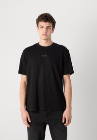 Black cotton T-shirt with a relaxed fit, featuring short sleeves and a crew neckline, and a small white "Calvin Klein" logo on the chest.