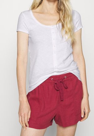 Woman wearing a white short-sleeve buttoned shirt tucked into red drawstring shorts, shown from shoulders to mid-thigh.