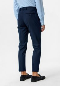 Marineblauwe broek met een slim fit, platte tailleband en twee achterzakken; gecombineerd met zwarte suède loafers en een lichtblauw shirt.