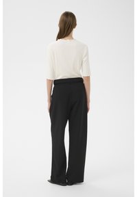 Biely rebrovaný top s vlnitými okrajmi, v kombinácii s čiernymi širokými nohavicami s vysokým pásom. Jednoduchý, minimalistický dizajn bez vzorov alebo akcentov.