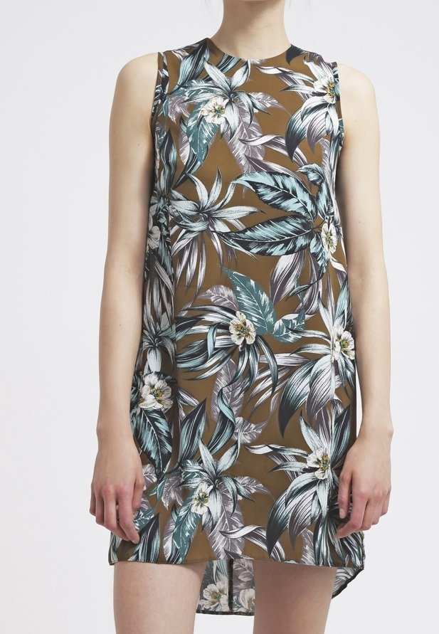 Hedvábné bezramínkové šaty s květinovým vzorem na hnědém pozadí, se velkými zelenými a bílými listy a bílými květy. Hladká tkanina s uvolněným střihem.