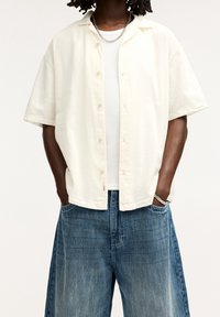 Lichtbeige kortermelig overhemd met knopen, gemaakt van een gestructureerde stof, gecombineerd met losse, vervaagde blauwdenim shorts met een wijde pijp.