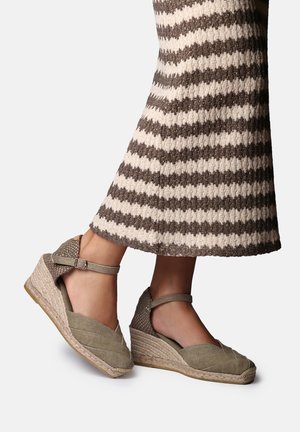 Kājām uzvilkti bēša toņa platformas espadrilu sandales ar potīšu siksniņām, kombinētas ar brūni krēmīgu svītraina raksta adītu kleitu.