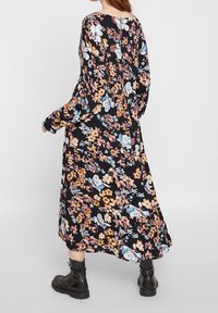 Blommig maxiklänning med långa ärmar, svart bakgrund, färgglada blommönster och knäppning bak, i kombination med svarta stövletter.