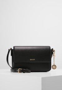 Borsa a tracolla nera in pelle con chiusura a pattina, hardware dorato e charm rimovibile. Tracolla regolabile per versatilità. Logo DKNY sul fronte.