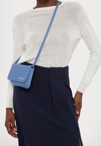 Un pull en tricot blanc léger associé à une jupe navy. Un petit sac bandoulière bleu présente une fermeture rabat et le nom de la marque "Marni."