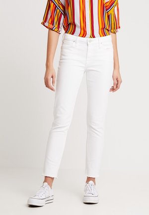 Jean skinny en denim blanc avec un ourlet effiloché, associé à une chemise à boutons multicolore à rayures et des baskets blanches.