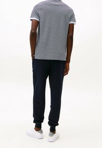 Polo à rayures en bleu marine et blanc avec des manches courtes, associé à un pantalon de jogger bleu marine. Des baskets blanches avec des accents gris complètent le look.