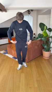 Navy sweat set with logo: long-sleeve crewneck and tapered pants. Roomy fit, soft cotton material, paired with silver sneakers, indoors.