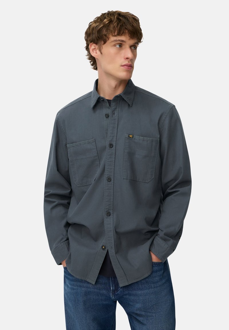 Grau button-up Hemd mit langen Ärmeln, zwei Brusttaschen und einem Kragen, aus einem glatten Stoff gefertigt. Getragen mit blauen Jeans.