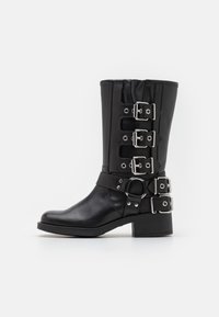 Svart läderstövel med en figursydd ovandel, fyra silverfärgade spännen på sidan, en rund metallaccent och en låg staplad klack.