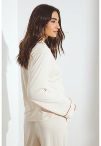 Crème-kleurige langmouwtop met een ontspannen pasvorm, met een ronde halslijn en contrasterende afwerking op de mouwen. Zachte, lichtgewicht stof.