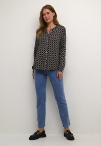 Camicia blu navy con un motivo geometrico color crema, maniche lunghe e colletto. Abbinata a jeans blu aderenti e mocassini neri.