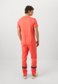 Koralfarvet kortærmet t-shirt og matchende joggers med sorte stribede manchetter, lavet af blød bomuldsblanding, med en afslappet pasform og enkelt design.