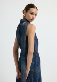 Vestido sin mangas de color azul oscuro con un detalle de bufanda larga y fluida en el cuello. Presenta patrones intrincados y un acabado de tela texturizada.