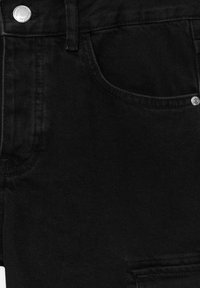 Los jeans de mezclilla negra presentan una textura suave, un diseño clásico de cinco bolsillos, herrajes metálicos plateados y costuras tonales.