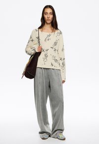 Haut à manches longues crème avec des motifs floraux noirs, associé à un pantalon gris ample et des chaussures bleues. Comprend un sac à main en cuir marron texturé.