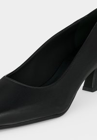 Escarpin noir en cuir pour femme, à talon bas carré et talon bloc, sur fond uni clair.