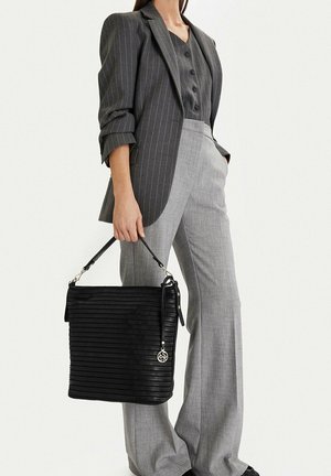 Mujer vestida con un blazer gris de rayas y pantalones grises, sosteniendo un gran bolso negro texturizado con un charm metálico.
