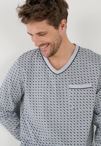 Maglietta grigia a maniche corte con motivo geometrico multicolore, scollatura a V, rifiniture blu scuro e una piccola tasca sul petto. Tessuto dalla consistenza morbida.