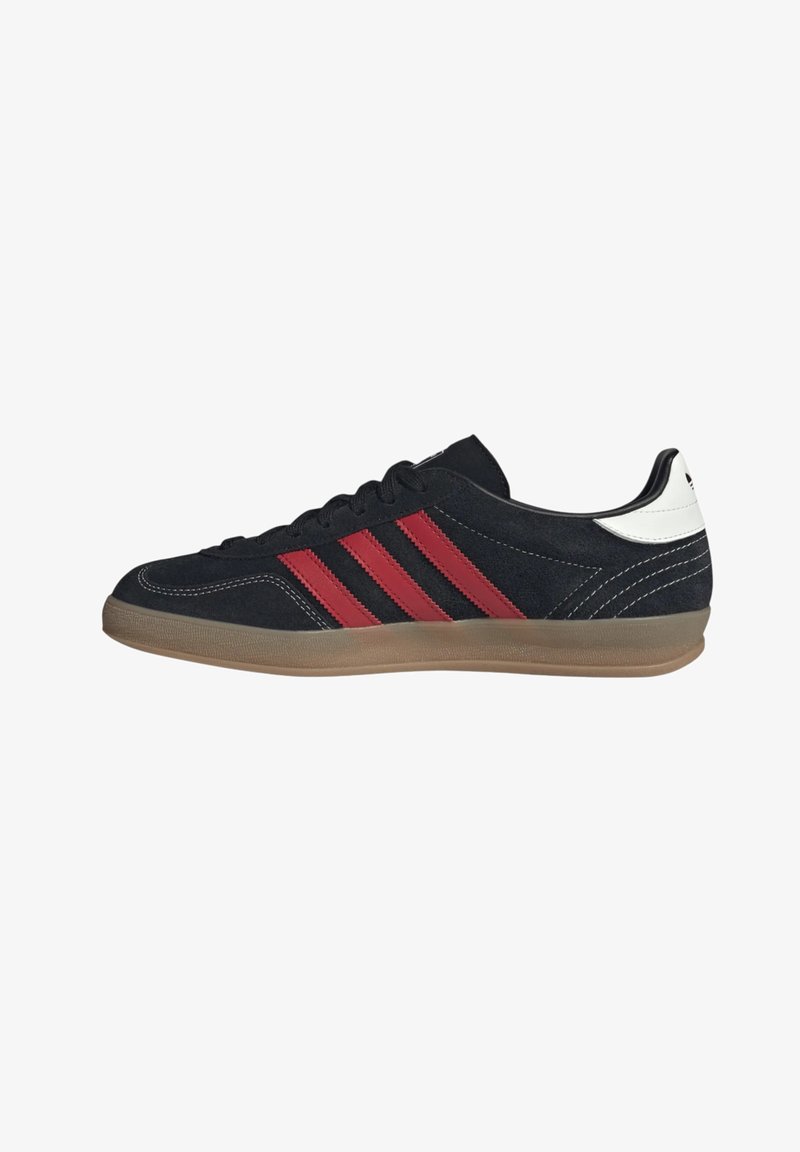 Baskets en daim noir avec des rayures rouges, une semelle gomme, des lacets noirs et un renfort talon blanc, vues de côté.